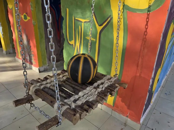 A black and gold basketball resting on a wooden swing hung on chains, in front of a painted UNITY mural wall