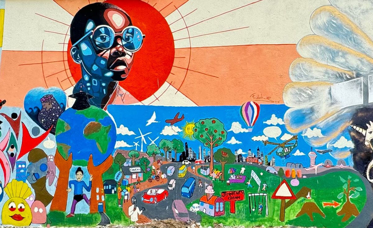 Painted mural of a figure in reflective sunglasses in front of a red sun, above a colourful landscape with a globe, wind turbines, houses and hot-air balloons.