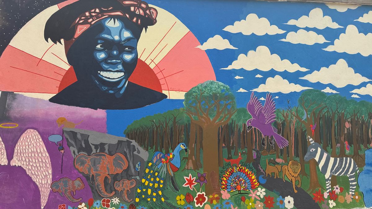 Painted mural of a smiling woman in a headwrap against a sunburst and clouds, above a forest with a zebra, birds and flowers.