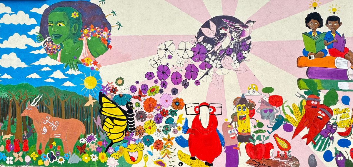Painted mural of a green-skinned figure, butterflies, flowers, a red bird and stacked books under pink sun rays and a blue sky.