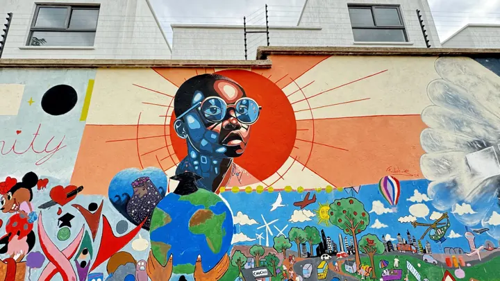 Wide mural of a boy in blue glasses before an orange sun, with a globe, trees and a city scene and the word Unity