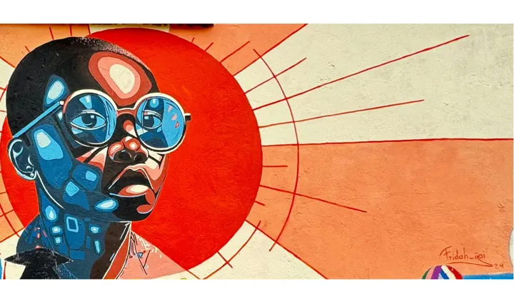 Close-up of a mural of a boy in round blue glasses against an orange sunburst, signed Fridah_iiai '24