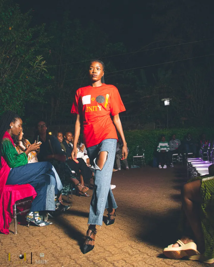 Model on a night runway in a red Unity tee and ripped blue jeans