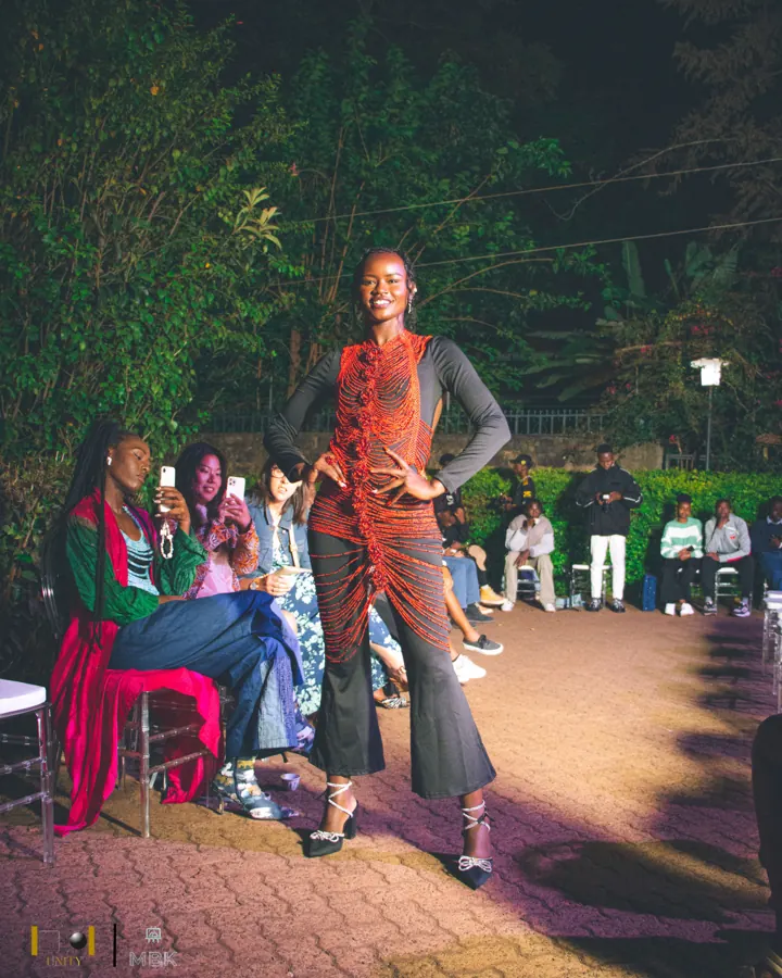 Model on a night runway in a red beaded top over a grey long-sleeve and flared trousers