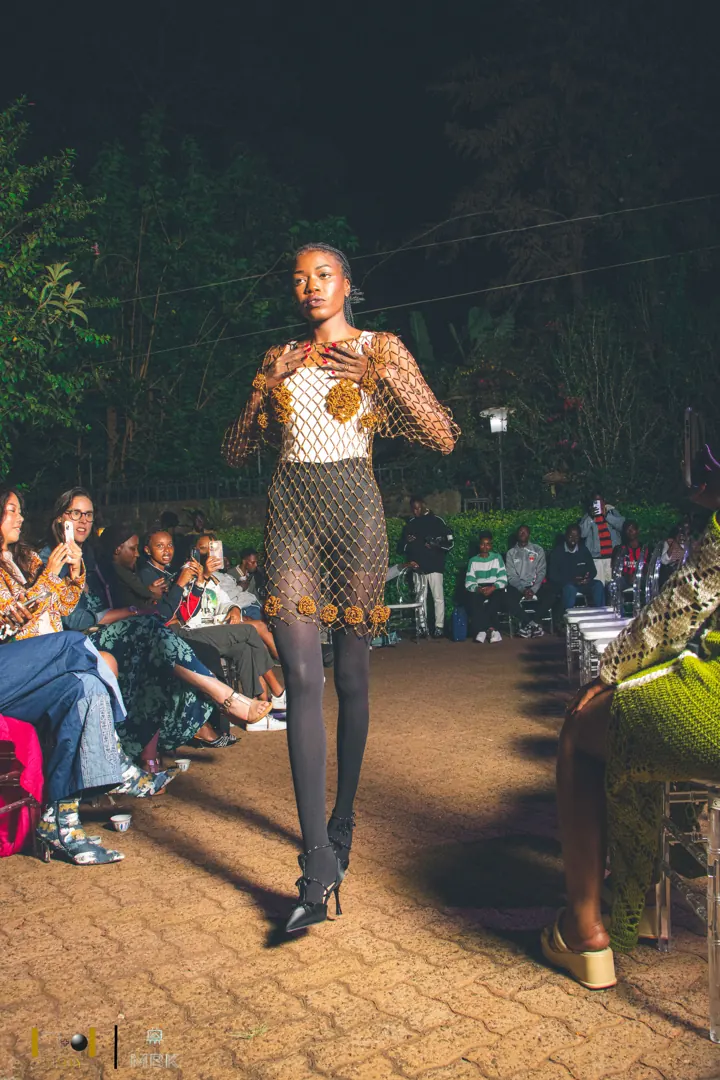 Model on a night runway in a crocheted net dress over a cream top