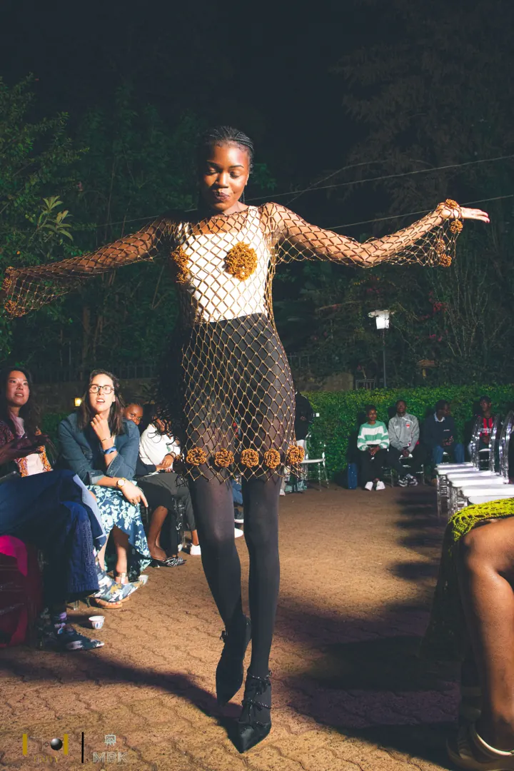Model on a night runway in a crocheted net dress, arms stretched out
