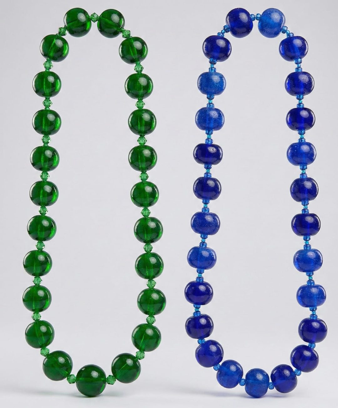 Two hand-forged glass bead necklaces on a light grey background: the Emerald Series in green beads with crystal spacers, and the Royal Cobalt Series in cobalt-blue beads