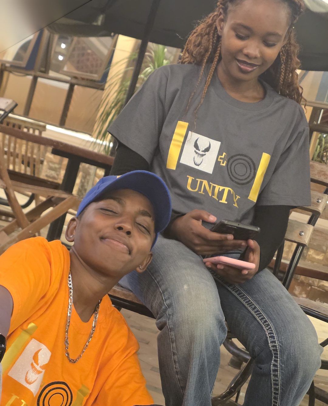 Two people wearing the Unity Halloween edition tees, one orange and one grey, with the gold UNITY print and a monster-face graphic