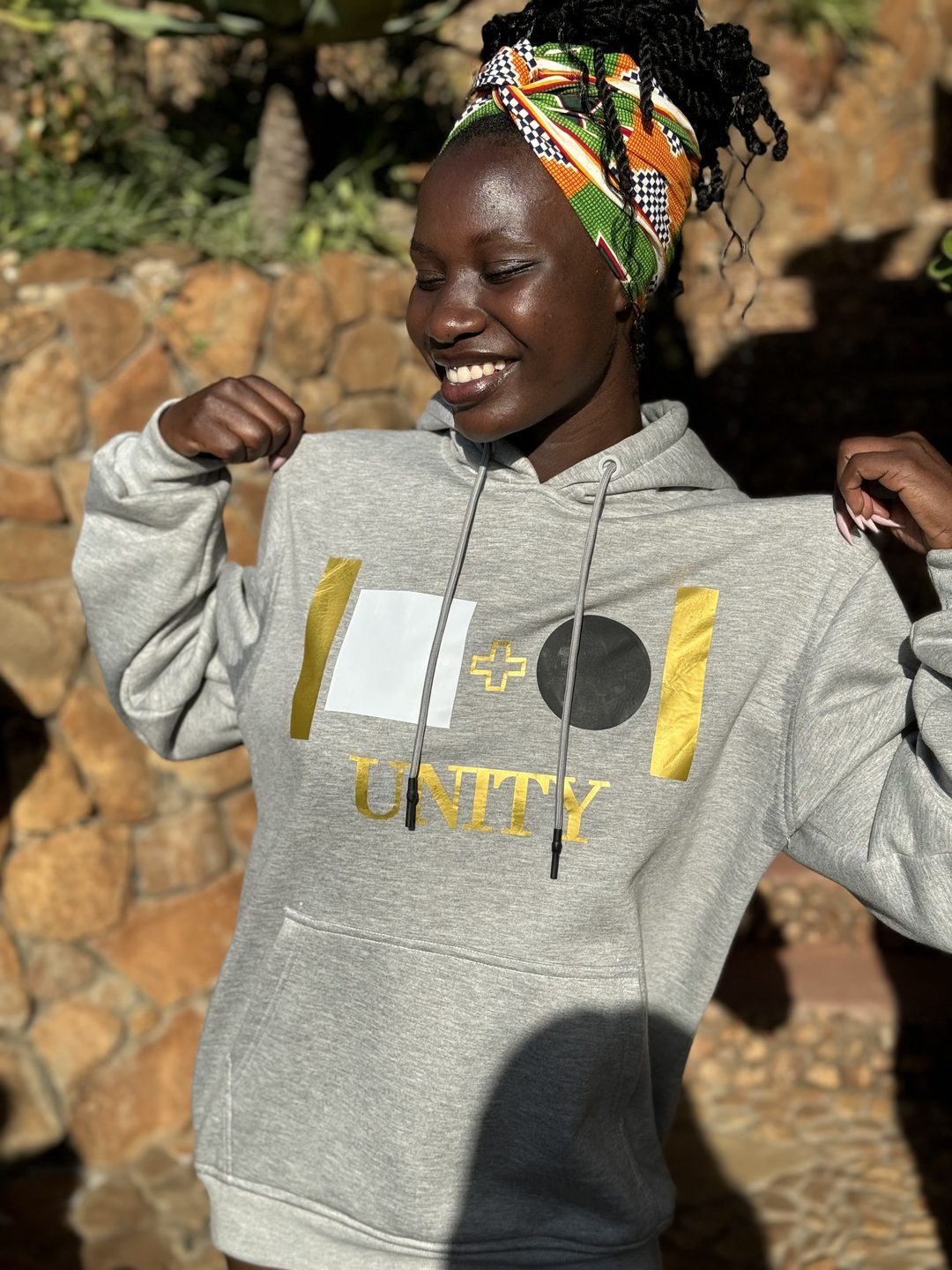 Model wearing the grey Unity hoodie, side angle, showing the gold UNITY print